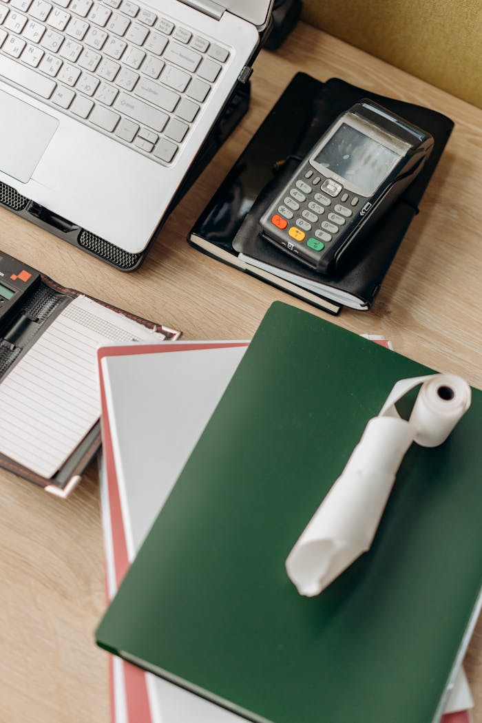 Overhead view of an office desk with laptop, payment terminal, and notebooks.